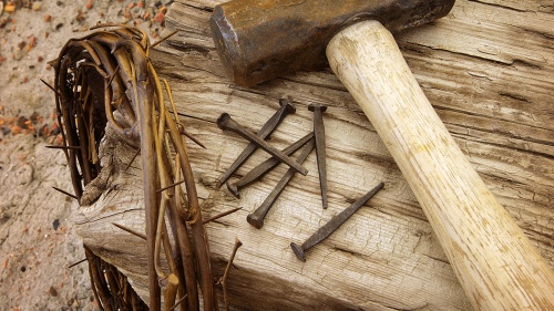 Photo illustration of a crown of thorns, old nails, hammer and wood beam.