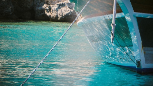 A boat in the water with a chain going down into the water attached to an anchor.