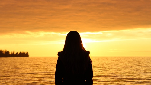 Woman standing by a body of water when the sun is setting.