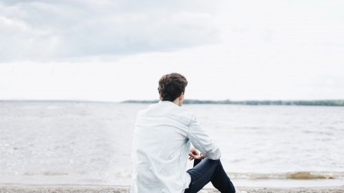 A young man sitting on the shore a lake - looking at the water.