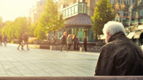 An old man sitting on a park bench looking down.