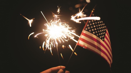 A person holding a sparkler and a small American flag.