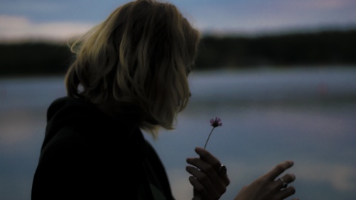 A woman holding a wilting flower in her hand.