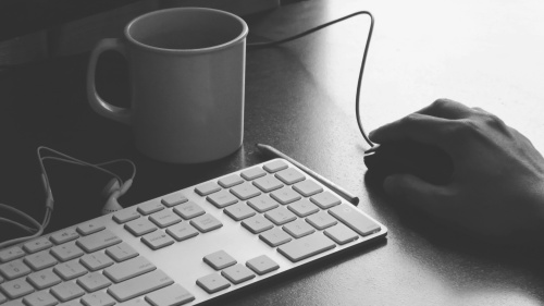 A coffee cup, keyboard and a mouse on a table.