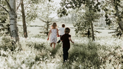 Three kids running through a field. 