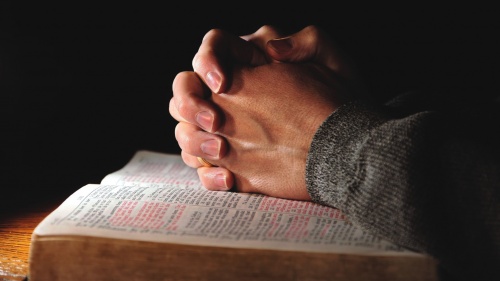 Clasped hands on top of an open Bible.