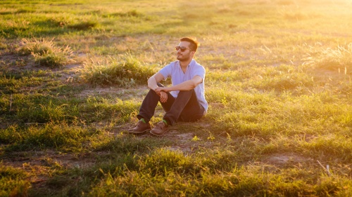 A man sitting in a field with the sun rays shinning.