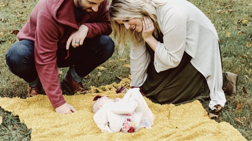 A dad and mom looking at their baby on a blanket.