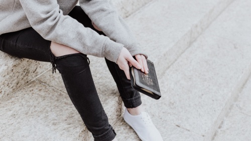 A woman sitting on concrete steps holding a Bible.