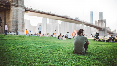 People sitting at a park by a large bridge.