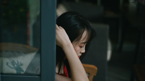 A woman looking depressed sitting by a window.