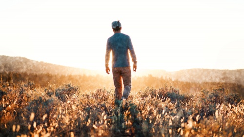 A man walking in a field with the sun rays shining on him.