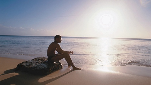 A man sitting on a rock on the beach.