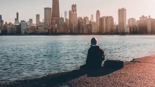 A person sitting at the edge of water looking at a city skyline.