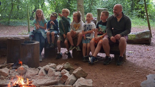 A group sitting by a campfire beneath a shelter