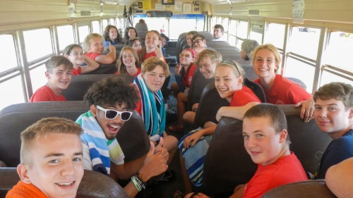 a group of teenagers sitting on a bus and turning to face the camera