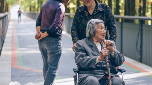 a woman pushing an older woman in a wheelchair while another woman watches