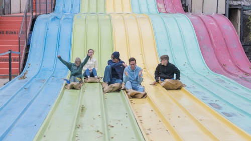 five teenagers sitting on a multi-lane, multi-color slide