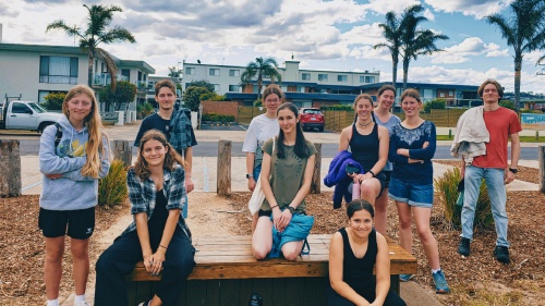 a group of teenagers standing and sitting outdoors in front of some buildings