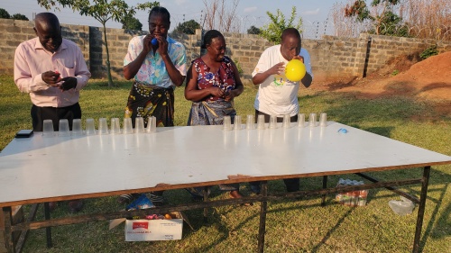 a group of four people playing games with cups and balloons at a table outdoors