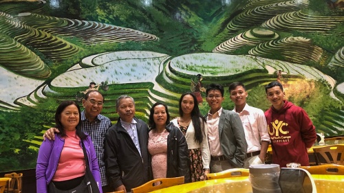 a group of people standing and smiling in front of a painting of a terraced green landscape