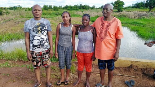 four people standing outside with a small pond in the background