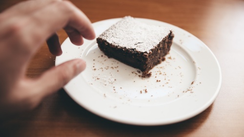 a hand reaching for a brownie on a plate