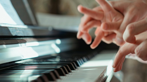 A piano instructor guiding the fingers of child on the piano.