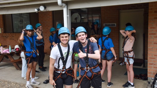 a group of teenagers with helmets and climbing harnesses standing in front of a building