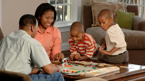 a couple and two boys sitting around a table and playing a board game