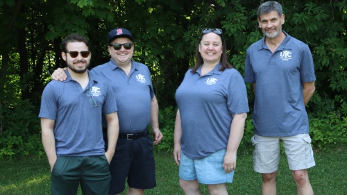 four people standing outdoors with matching camp shirts