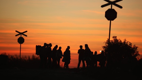 Silhouette of people standing at a railroad creossing.