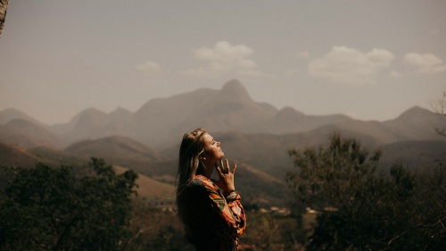 a woman with folded hands standing outdoors amidst mountain scenary