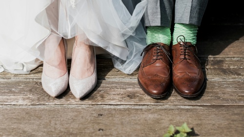 two pairs of feet, one wearing bridal shoes, one wearing men's dress shoes