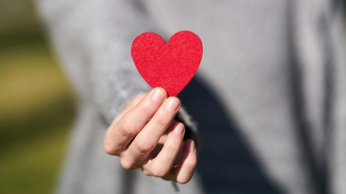 a woman's hand holding up a red paper heart