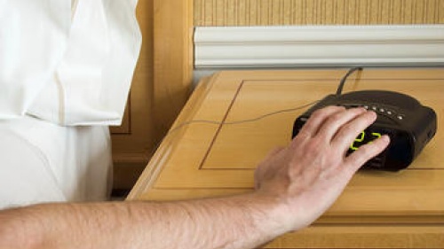 A man pressing the snooze button on an alarm clock.