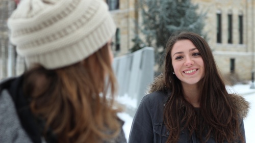 Two young adult women talking to each other while being outside in the cold.