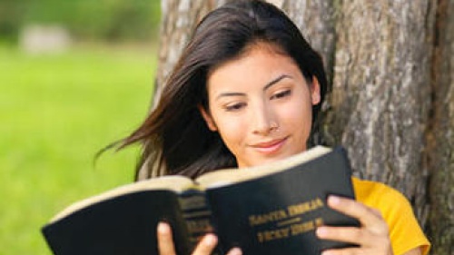 A young woman reading a Spanish version of the Bible (Santa Biblia).