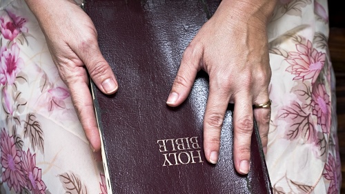 A Bible resting on the lap of a woman. Her hands on on top of the Bible.