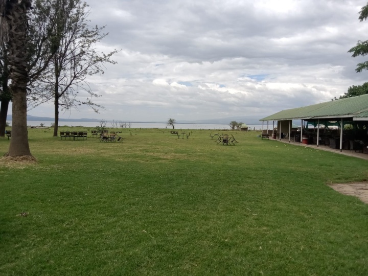 picnic benches and a shelter built on an expanse of green lawn under a cloudy sky with water and mountains in the distance