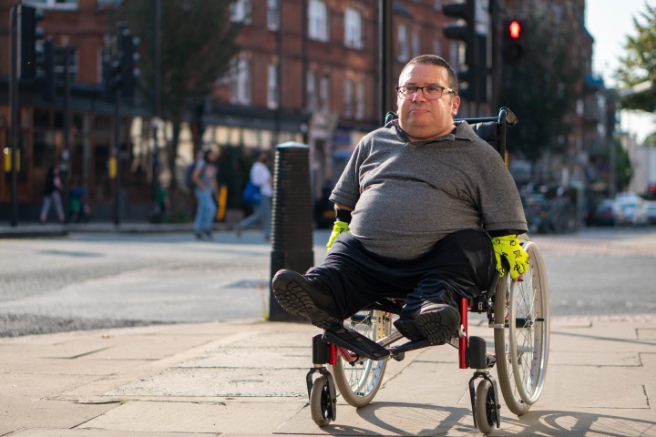 A man in a wheelchair going down a city street sidewalk.