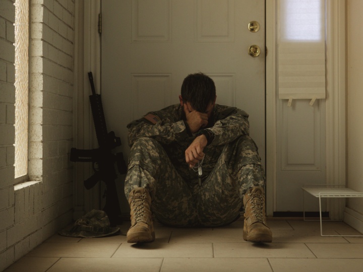 a soldier wearing camo sitting on the floor inside a house with his head in his hand