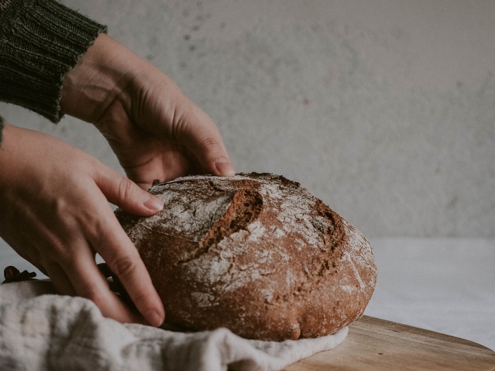 a pair of hands placing a loaf of bread onto a wooden cutting board