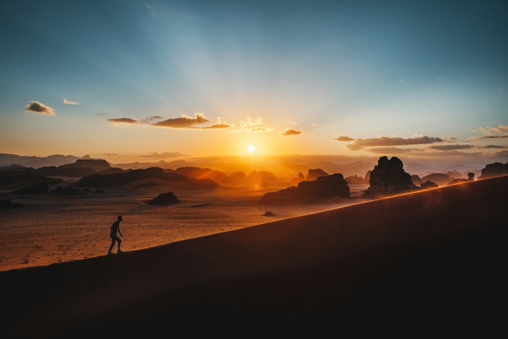 a man walking up a large hill with a sunset in the background