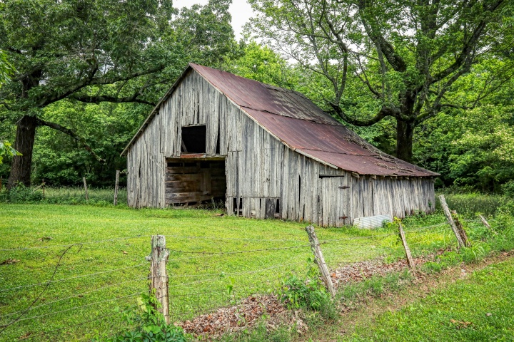 old gray barn surrounded by green grass and green trees