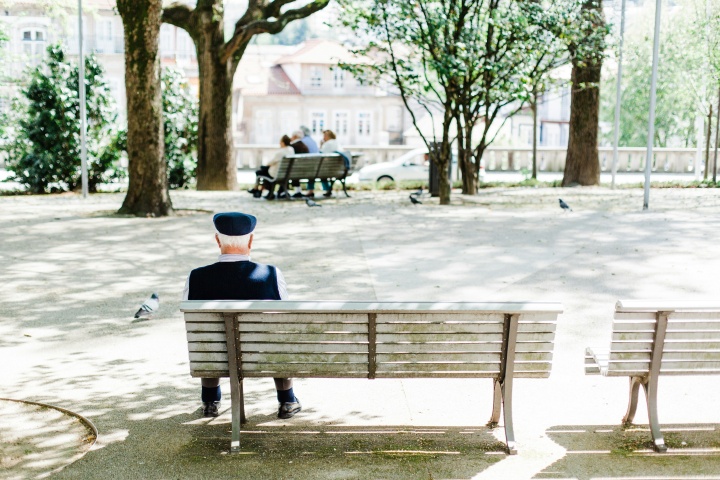 an elderly man sitting on a bench in a park