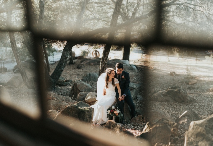 a bride and a groom sitting outdoors seen through a window pane