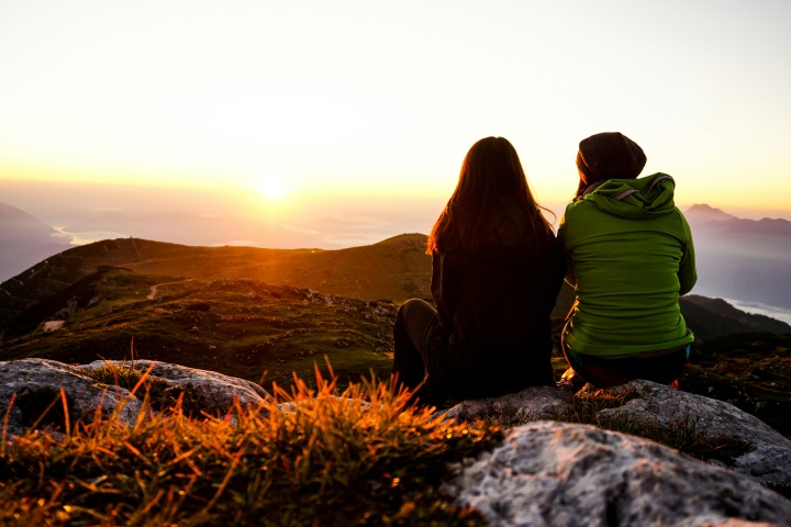 two women seated and silhouetted against the sunset with mountains in the distance