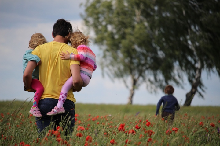 A father walking in field carrying two daughters.