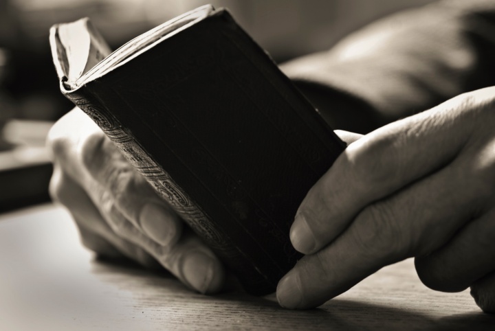 A man's old hands holding a small Bible.